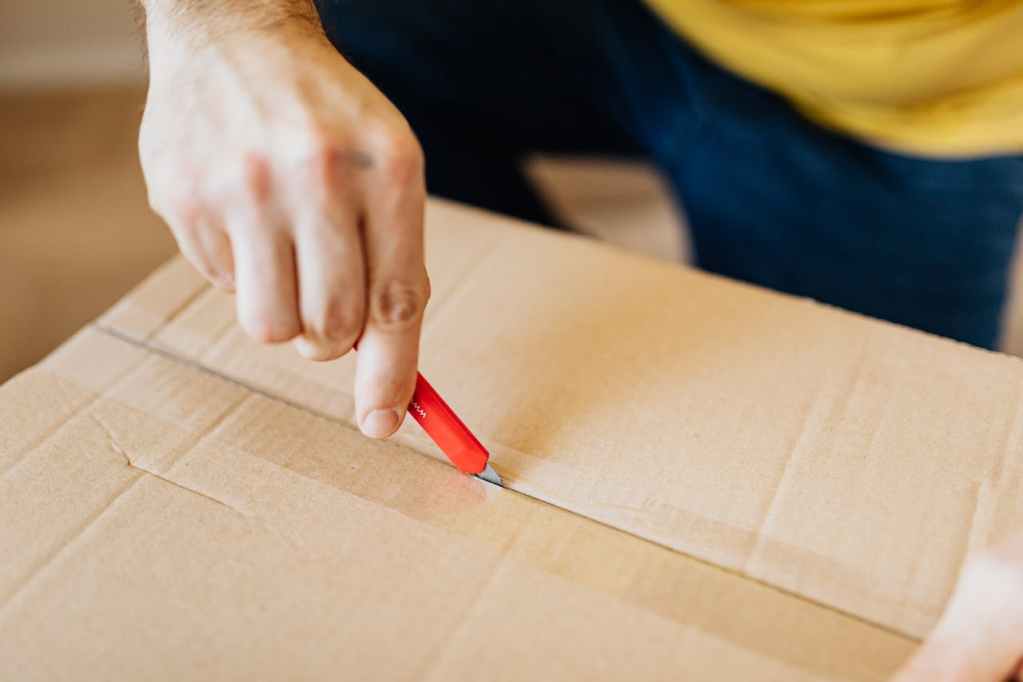 man using box cutter to open moving box
